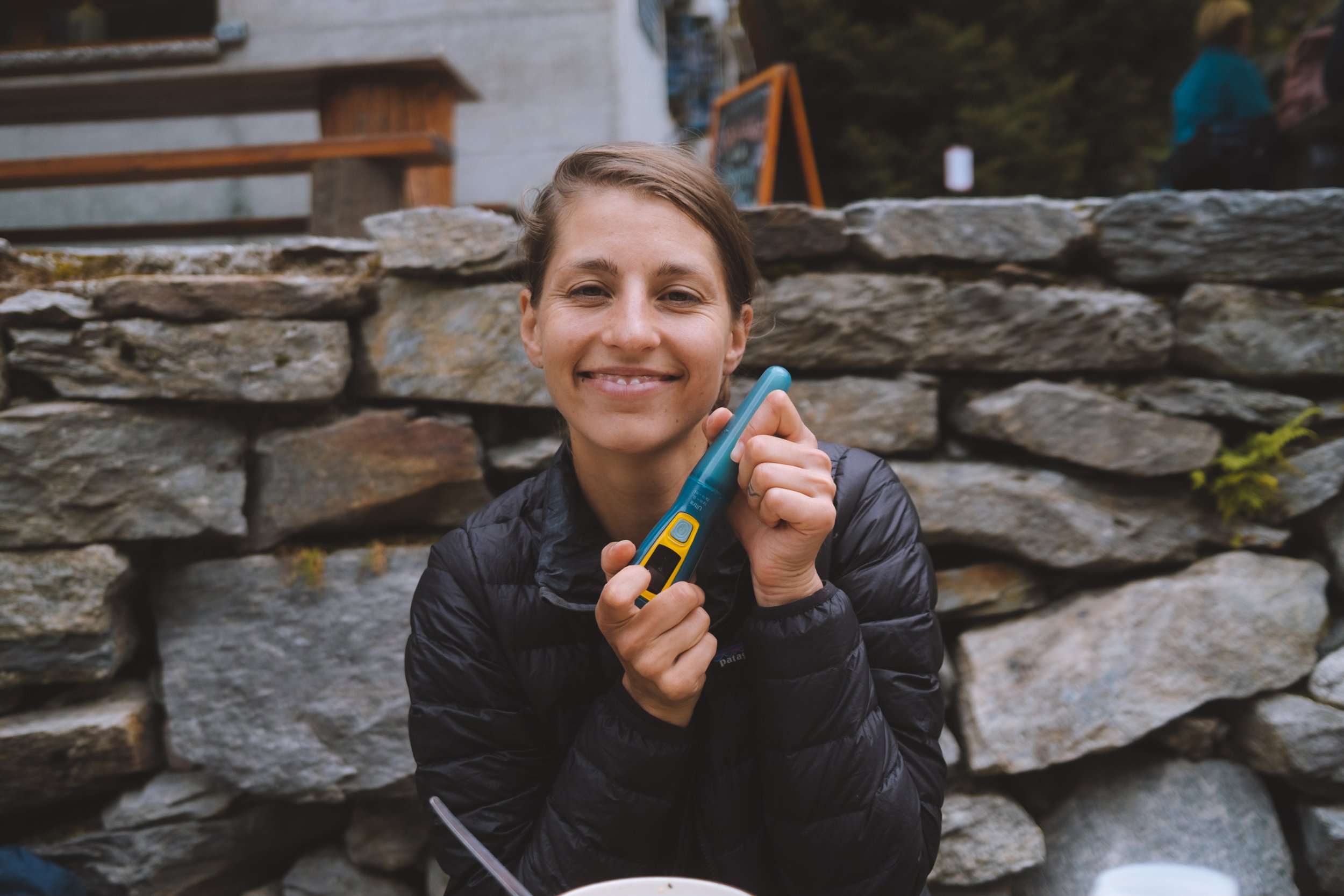 Andrea in black holding a green and yellow steripen in her hand outside with a stone wall in the background 